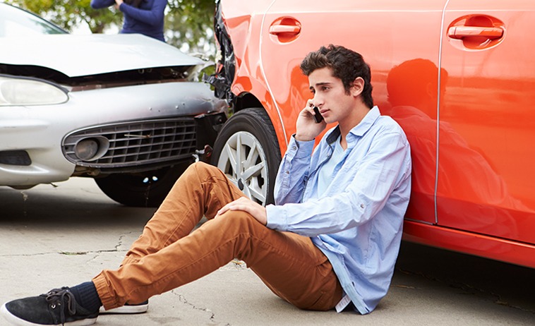 Photo of a man sitting on the ground after a crash as he makes a call